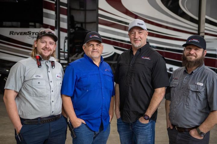Four men standing in front of an RV, wearing work shirts and hats.
