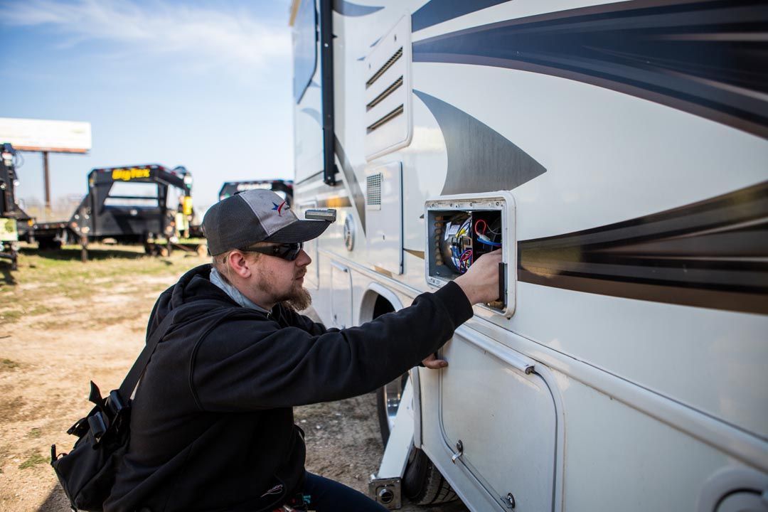 Man in cap opens a compartment on a white RV exterior. The man is outdoors.