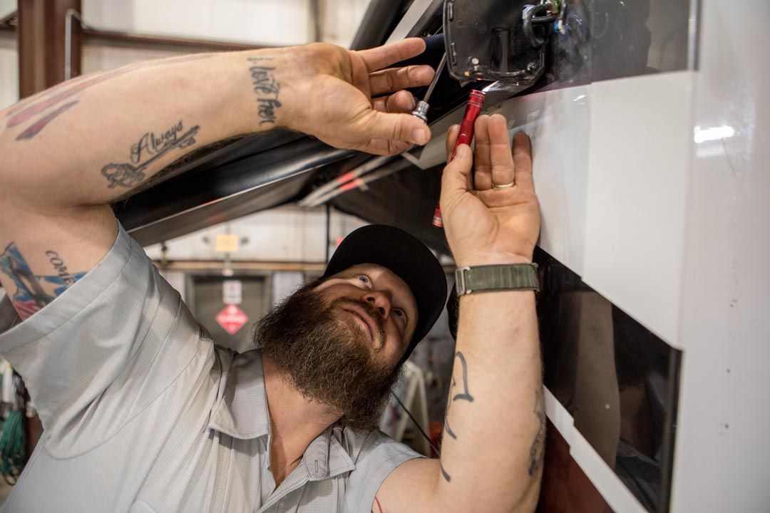 Mechanic with tattoos works on vehicle, using a red tool.