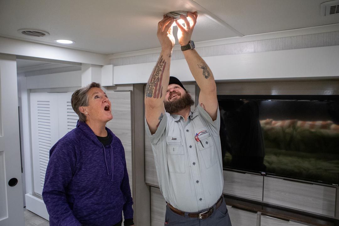Man changing a lightbulb with a woman watching; interior setting, bright overhead light.