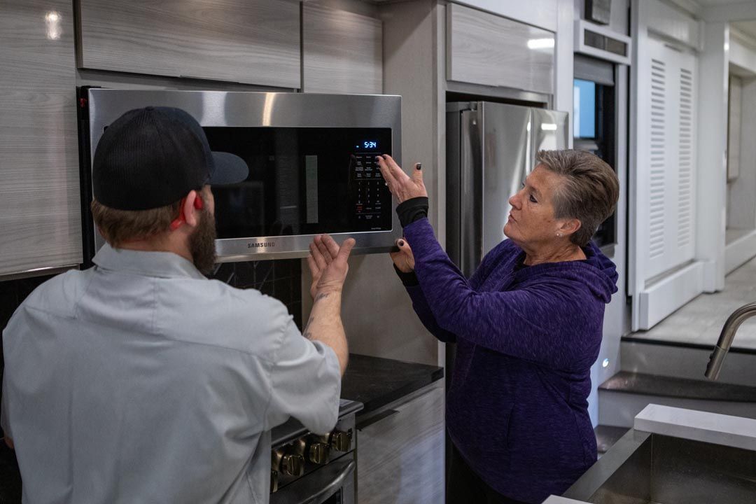 Man and woman looking at a microwave in an RV kitchen. Man points up, woman points at buttons.