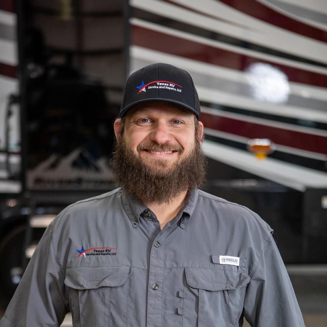 Man in cap and work shirt, smiling, standing in front of RV.