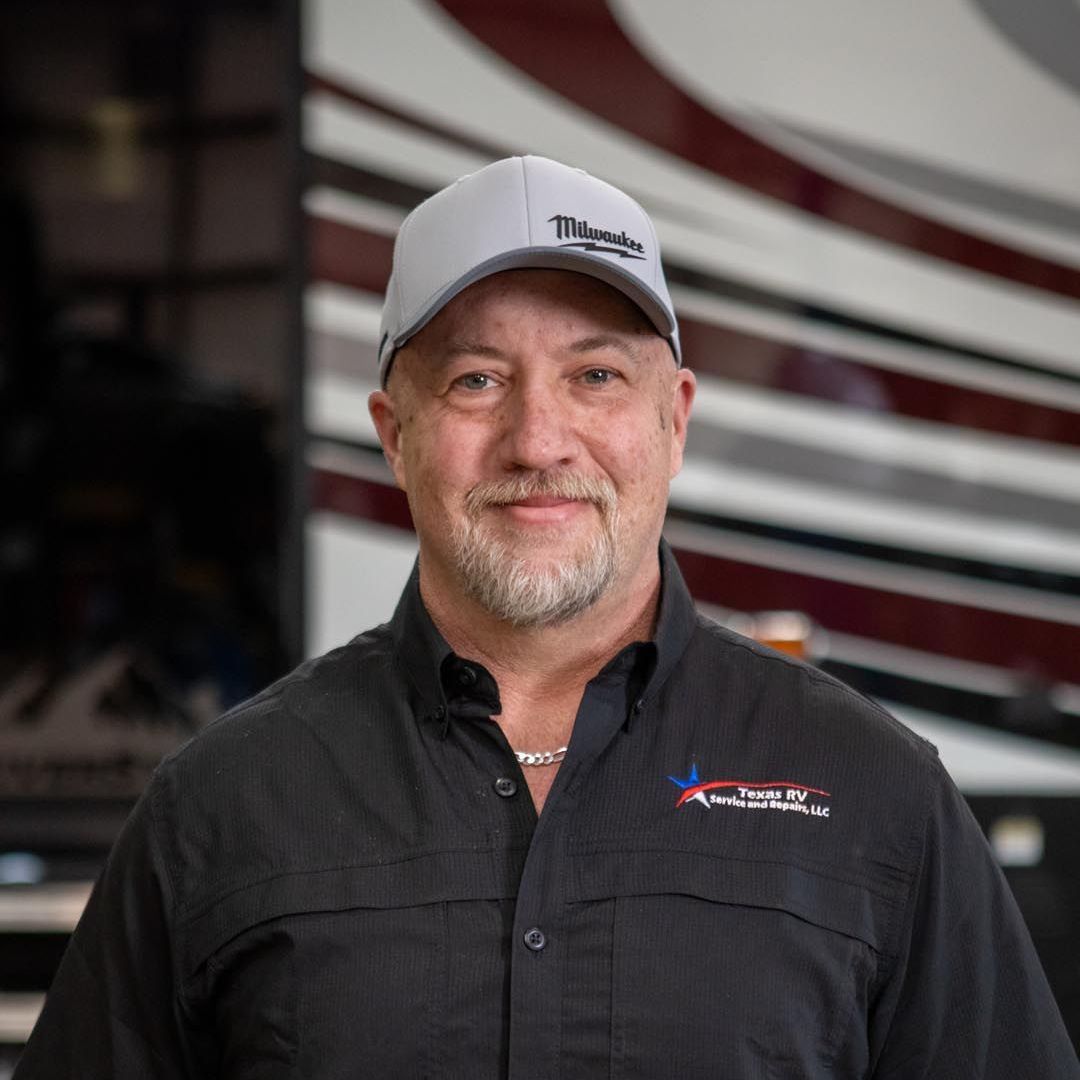 Man in a gray cap and black shirt smiles at the camera in front of a recreational vehicle.