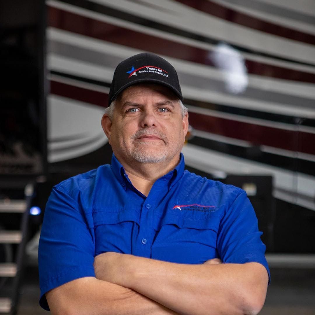 Man in blue shirt and baseball cap with crossed arms, RV background.