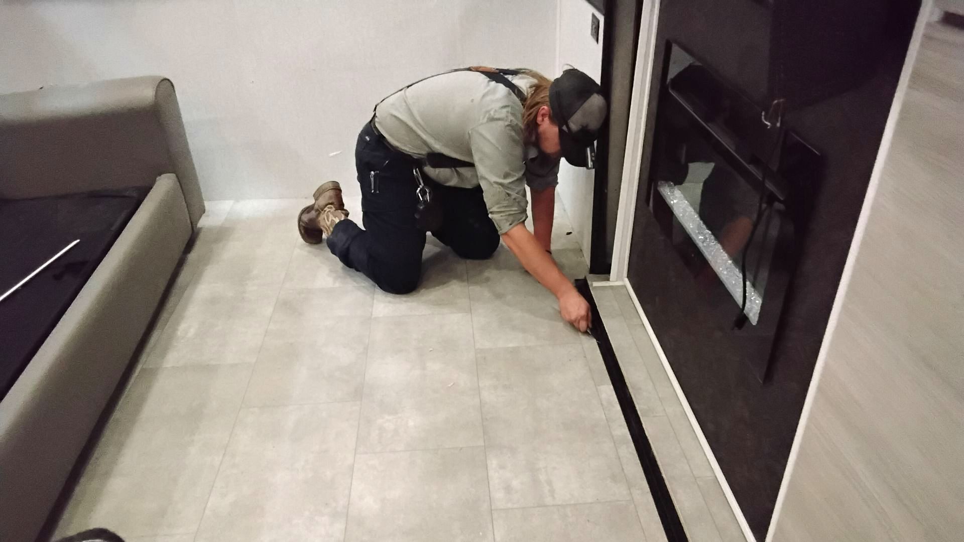 Person kneels, installing black trim along a doorway in a room with light flooring and a sofa.