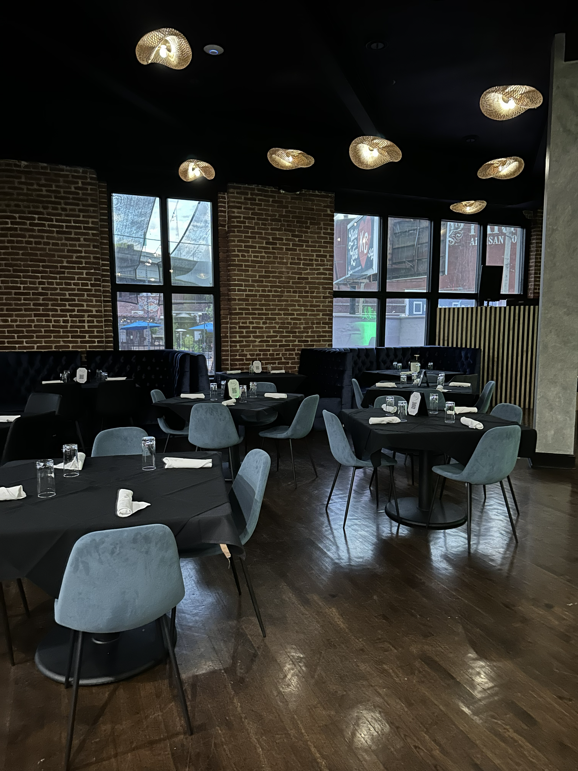 Empty modern restaurant dining room with dark tables, gray chairs, wood floors, and large windows.