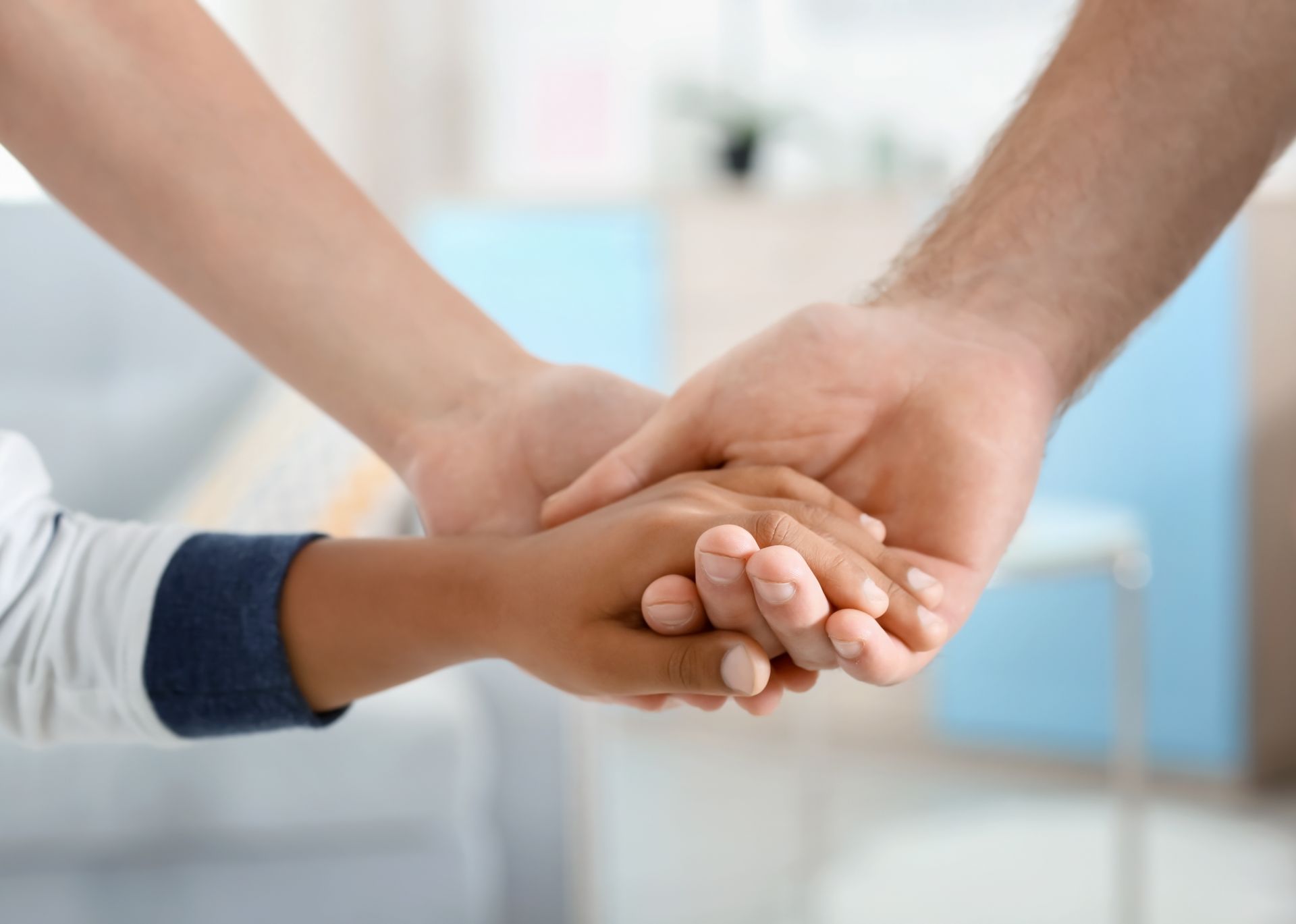 Hands of three people, of differing skin tones, holding each other.