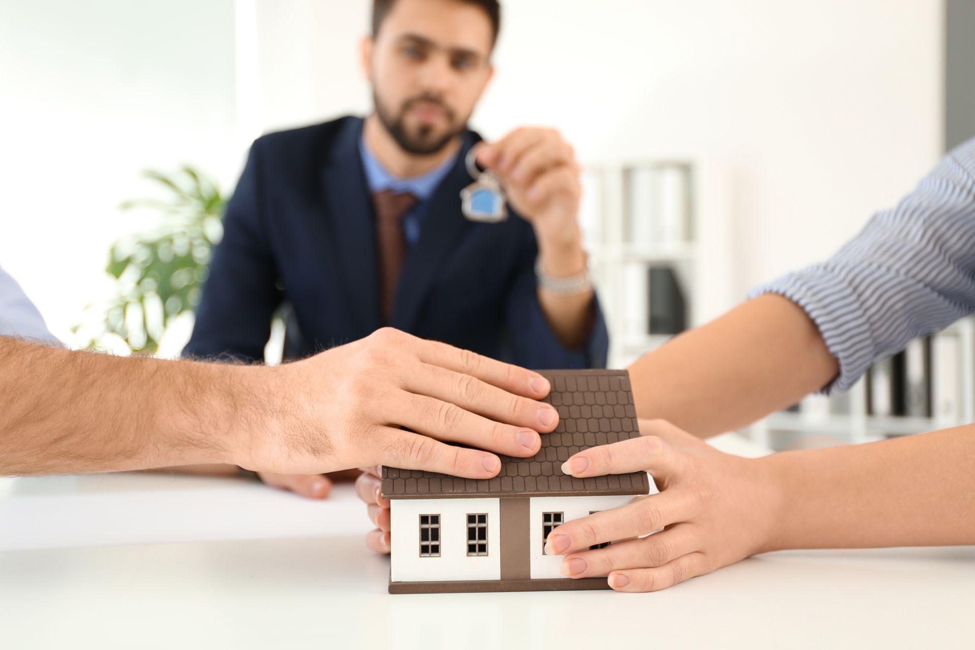 People arguing over a house model, with a man holding keys in the background.