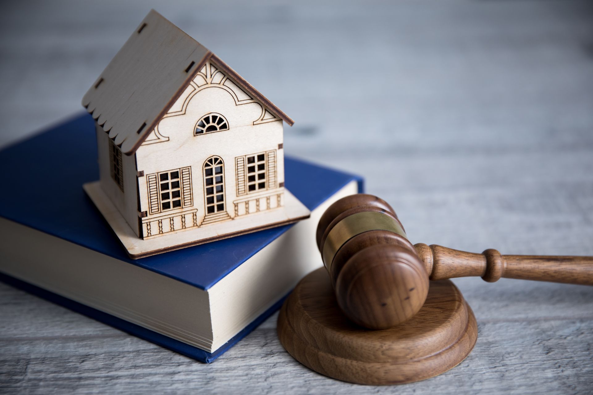 Wooden house model on a book next to a gavel and sound block, representing real estate law.