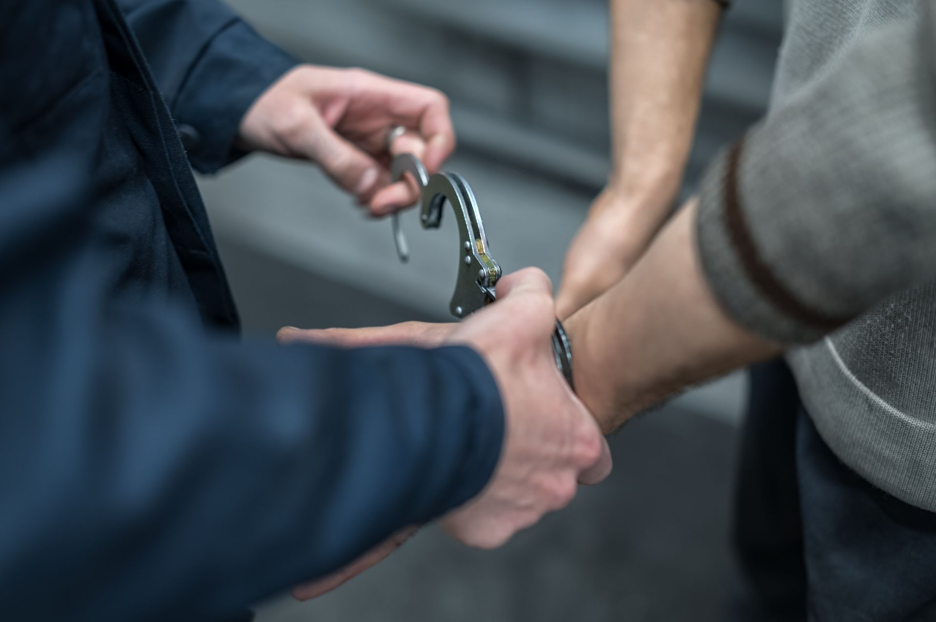 A person is being handcuffed by another person, indoors. One person wears a suit.