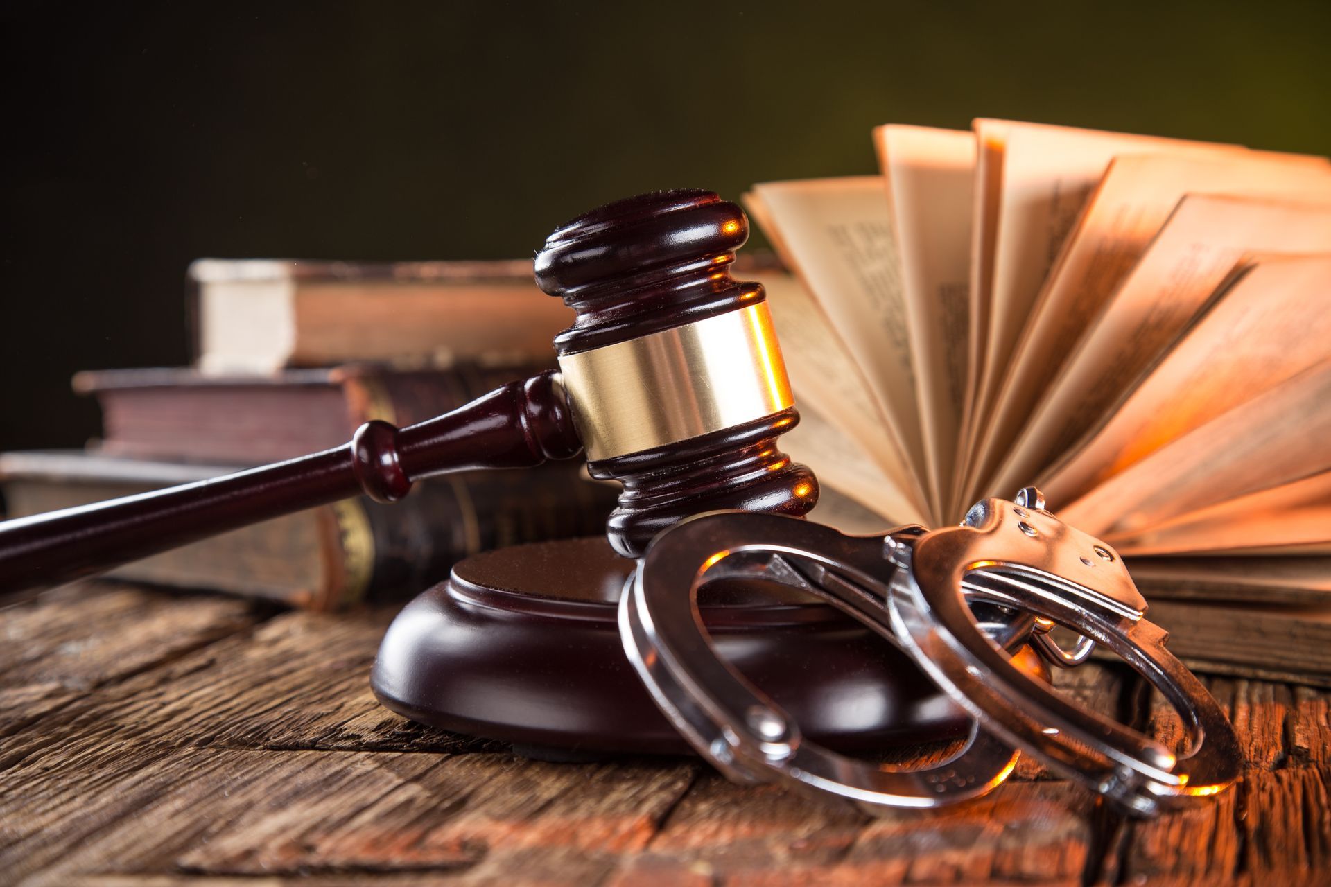 Gavel, handcuffs, and open book on a wooden surface, suggesting legal proceedings.