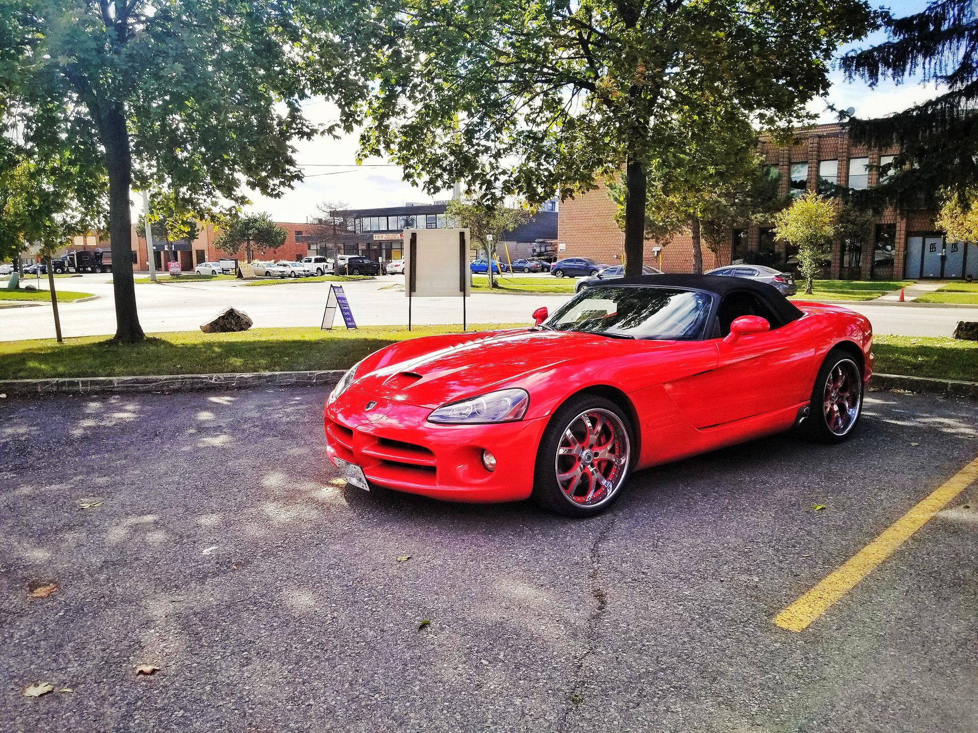 Red Dodge Viper convertible parked in a lot under trees, sunny day.