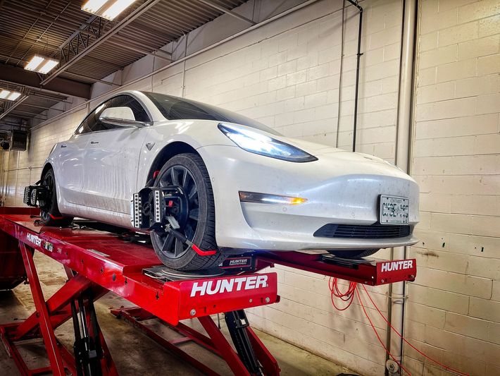 White Tesla on a red Hunter alignment lift in a garage, being serviced. | Mecano Autoworks