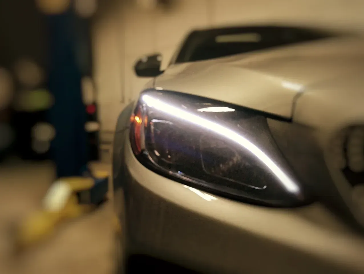 Silver car headlight illuminated in garage. | Mecano Autoworks