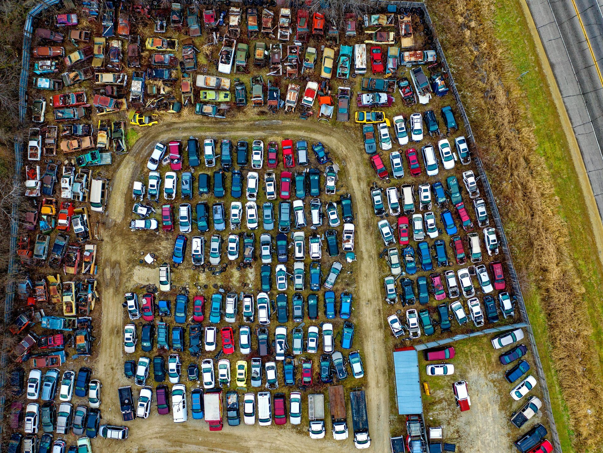 Vue aérienne d'une casse automobile bondée, avec des centaines de véhicules alignés en rangées et une autoroute à proximité.