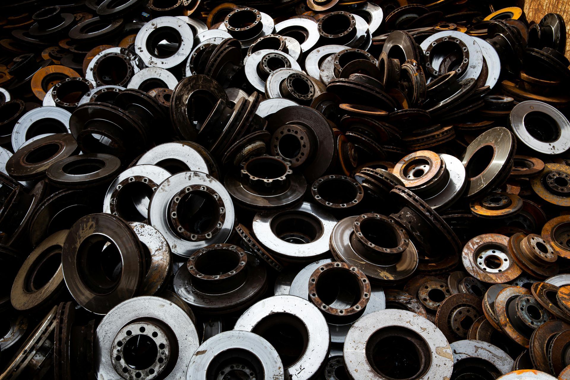 Un gros tas désordonné de disques et de rotors de freins automobiles métalliques usagés, présentant divers états d'usure.