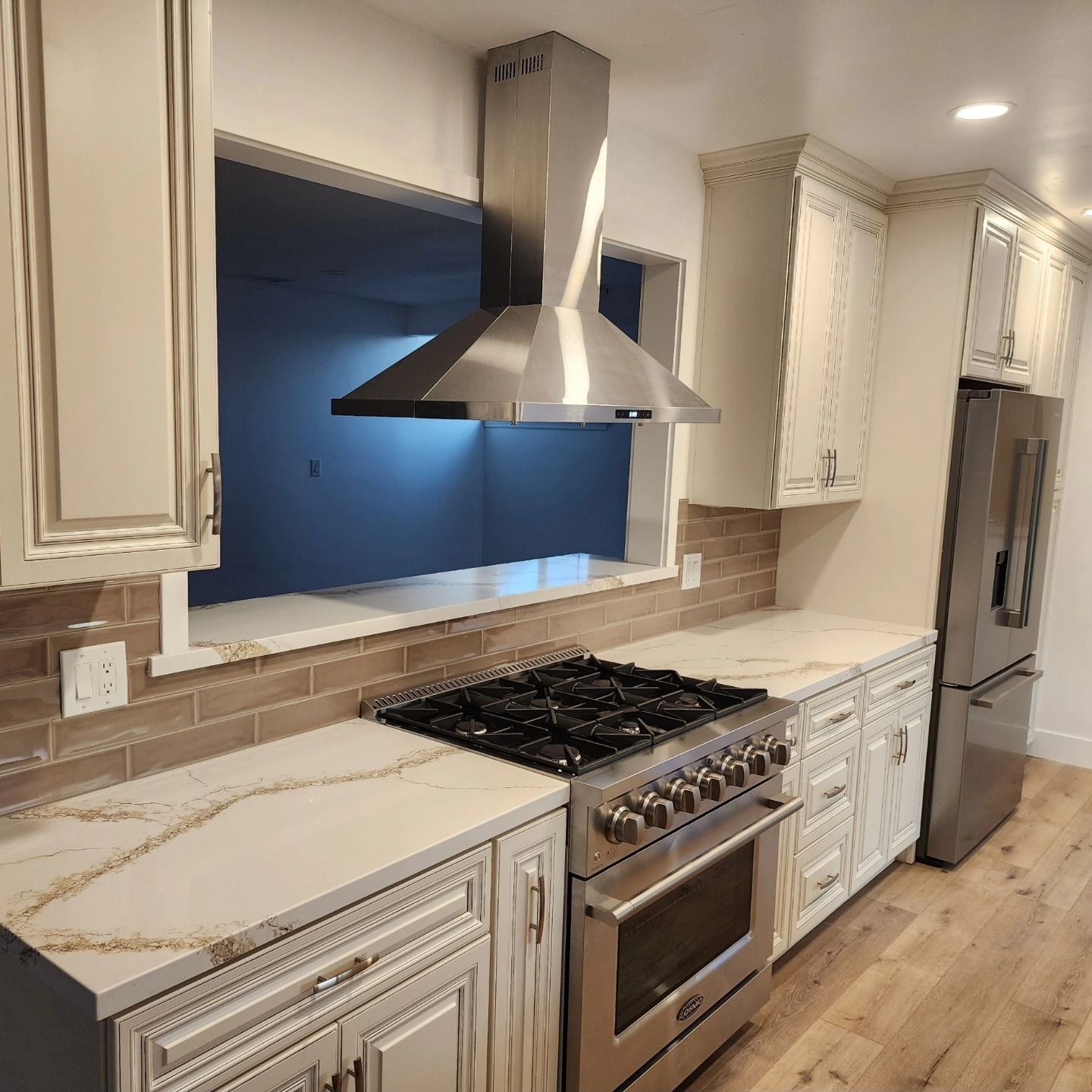 Modern kitchen with white cabinets, stainless steel stove and hood, wood floor, and blue-lit window backsplash