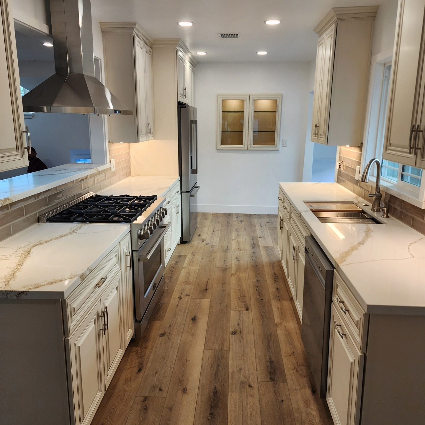 Bright modern galley kitchen with white cabinets, marble counters, stainless stove, and wood floors