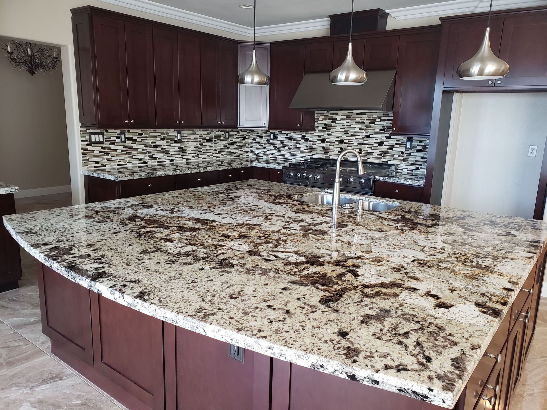 Modern kitchen with large granite island, dark cabinets, mosaic backsplash, and pendant lights