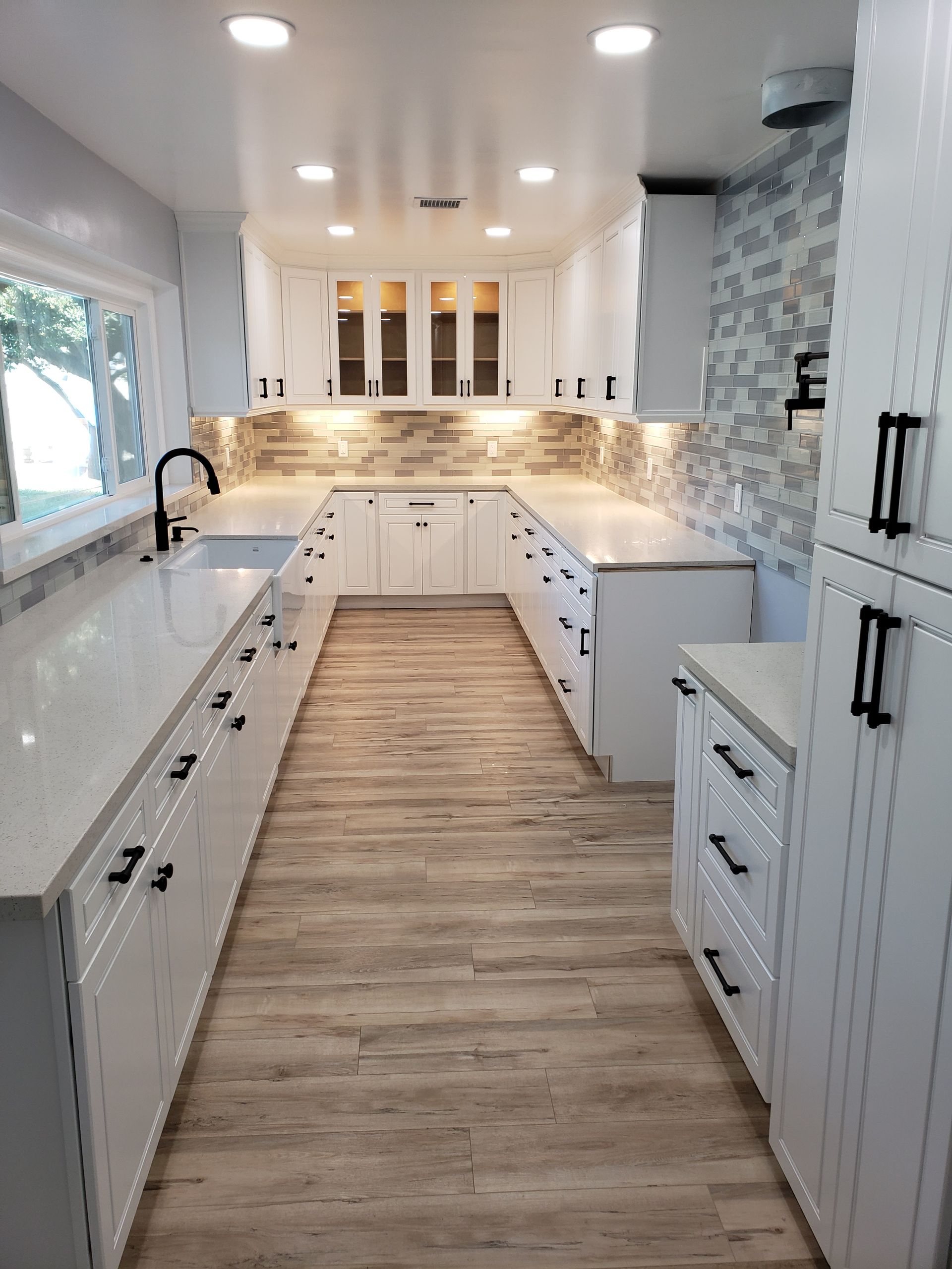 Bright white galley kitchen with wood floor, subway tile backsplash, and black hardware lighting.