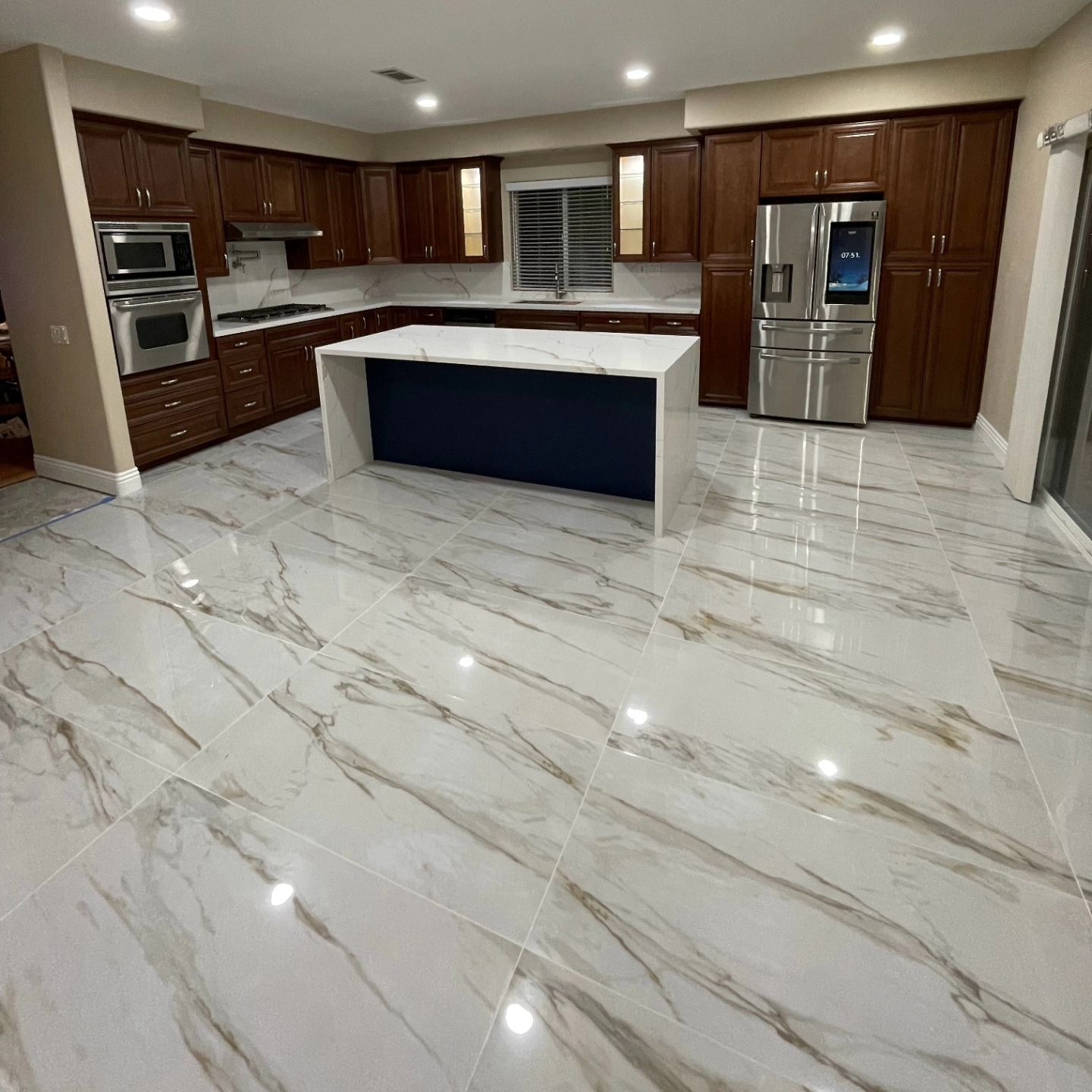 Spacious kitchen with dark wood cabinets, white countertops, and marble-patterned floor. Includes an island with navy blue base.