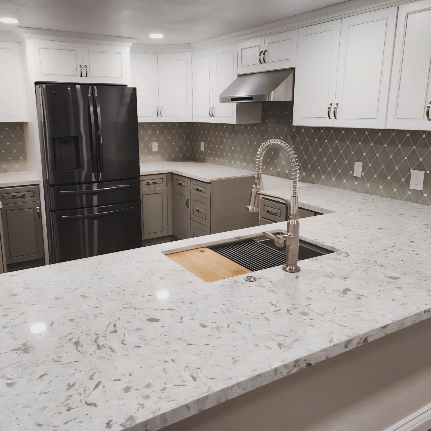 Modern white kitchen with black fridge, speckled countertops, and stainless sink faucet