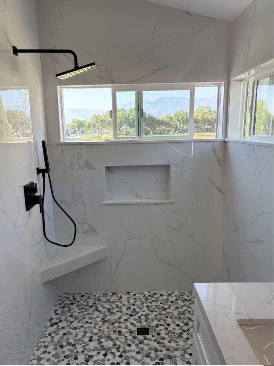 Modern bathroom shower with marble-look walls, mosaic floor, black fixtures, and a window view outside