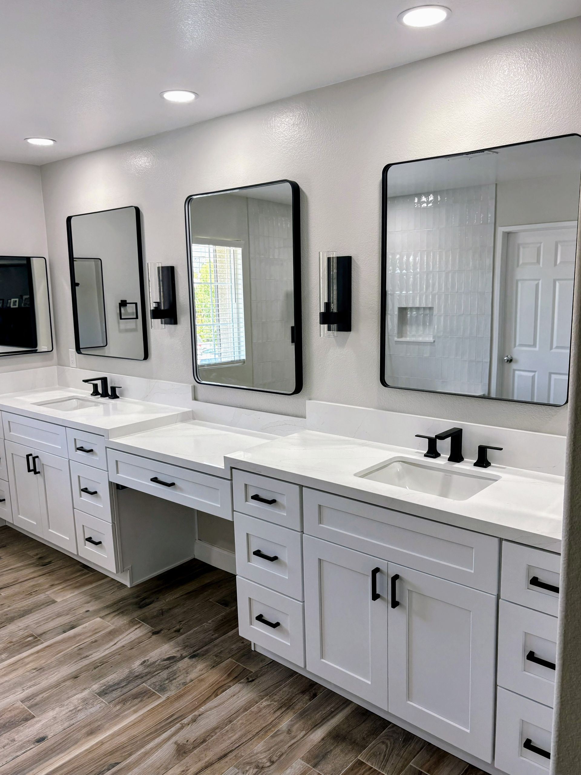 Modern bathroom vanity with double sinks, mirrors, white cabinets, and wood-look flooring