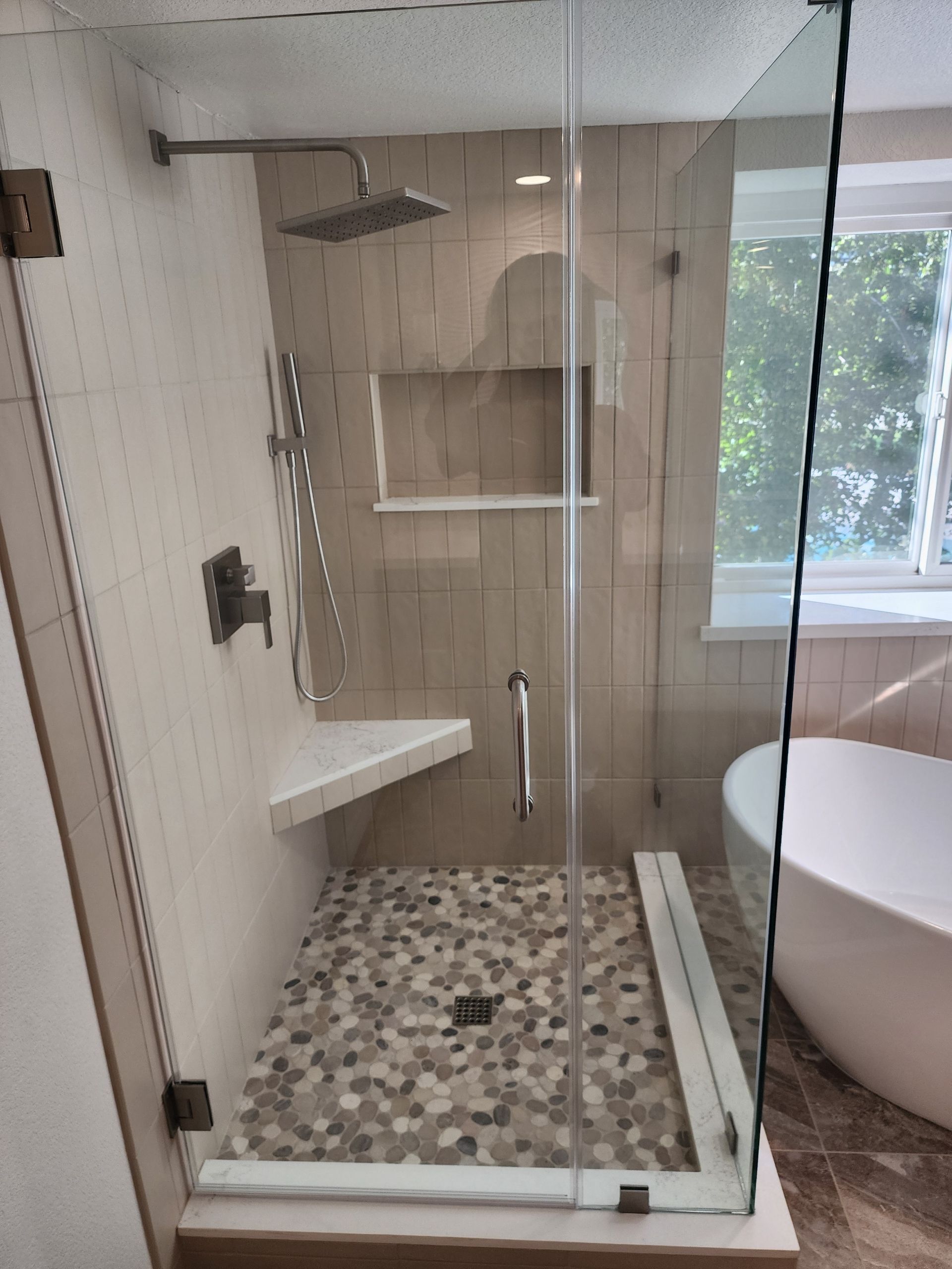 Glass walk-in shower with mosaic tile floor, built-in bench, and shelf in a modern bathroom