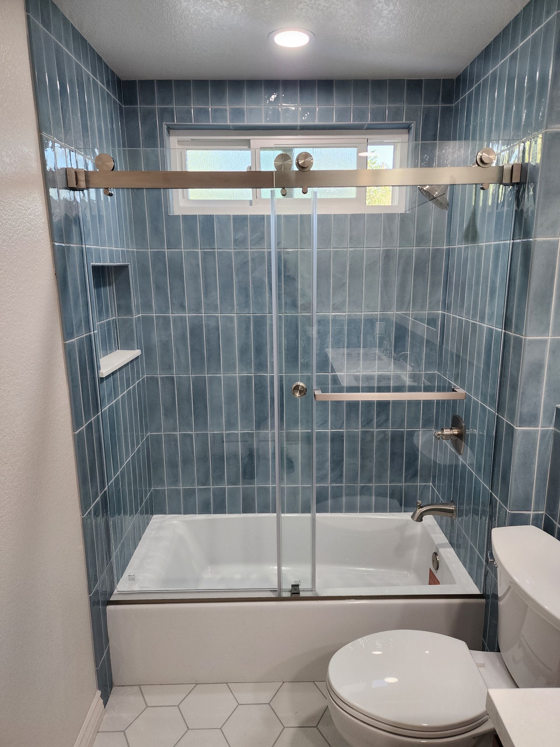 Small tiled bathroom with a glass walk-in shower, white tub base, and toilet in front.