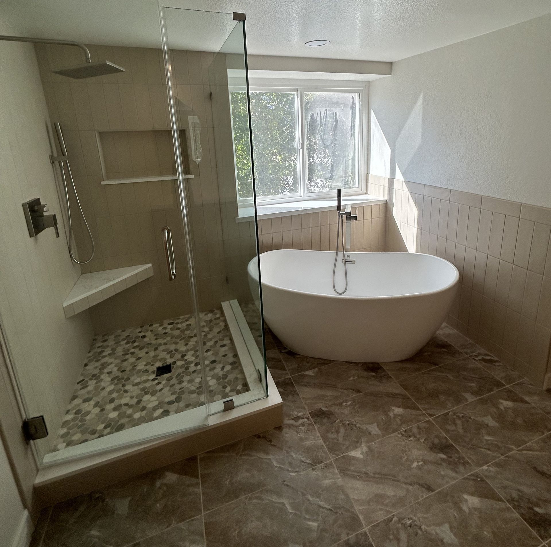 Modern bathroom with glass shower, freestanding tub, marble floor, and window light