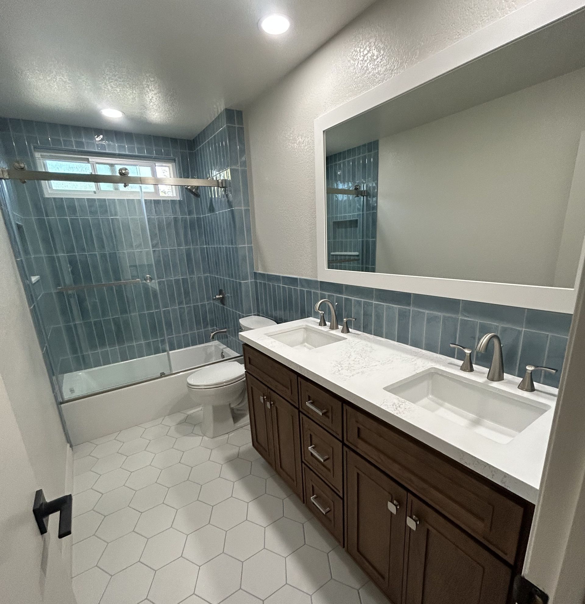Modern bathroom with double vanity, large mirror, hex tile floor, and blue-tiled shower/tub area