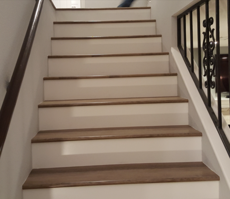 Indoor staircase with white risers, wood treads, and dark handrails leading upward