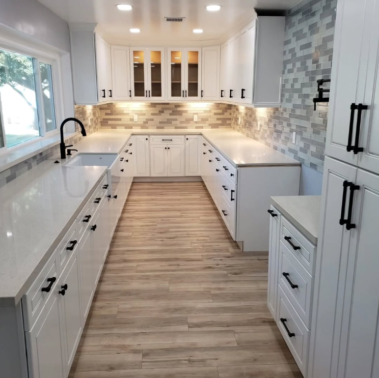 Bright modern white kitchen with dark hardware, wood floors, and a large island walkway