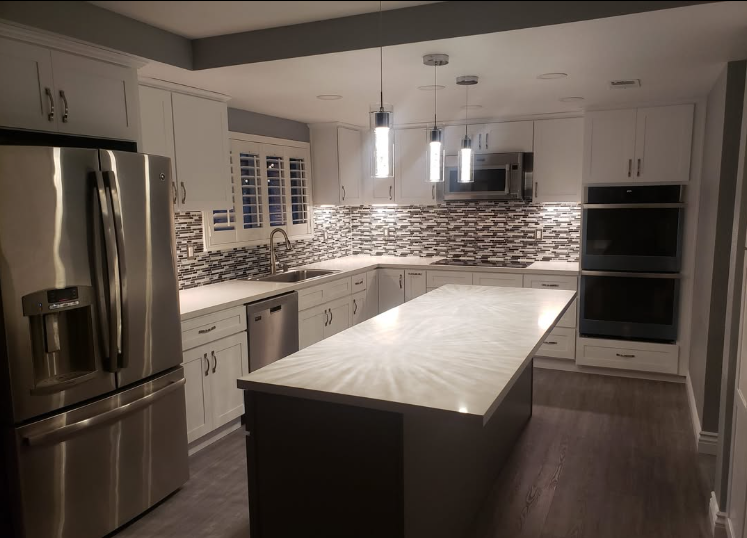 Modern white kitchen with stainless steel appliances, large island, mosaic backsplash, and pendant lights