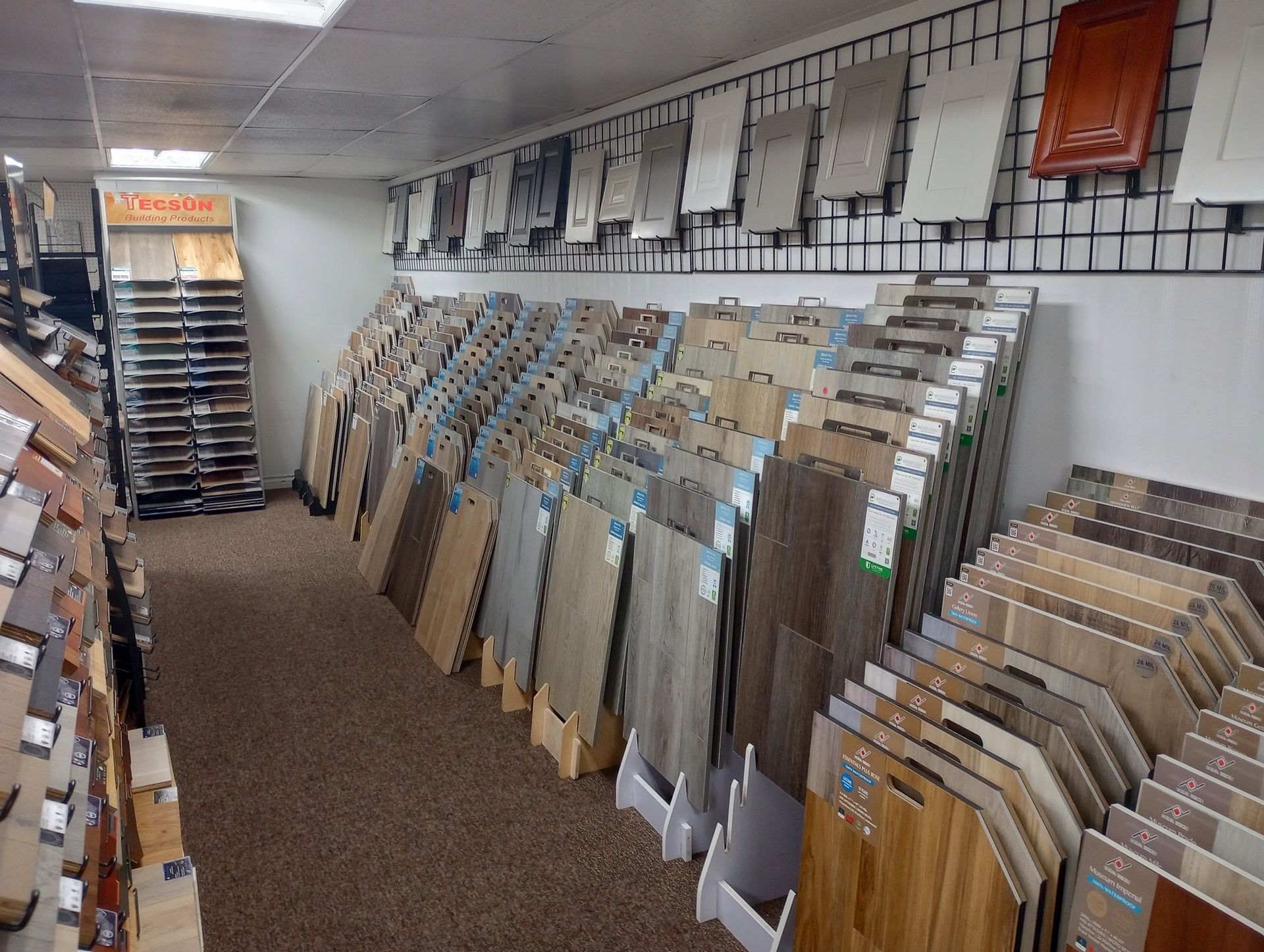 Tile showroom with rows of sample boards and wall-mounted displays in a narrow aisle