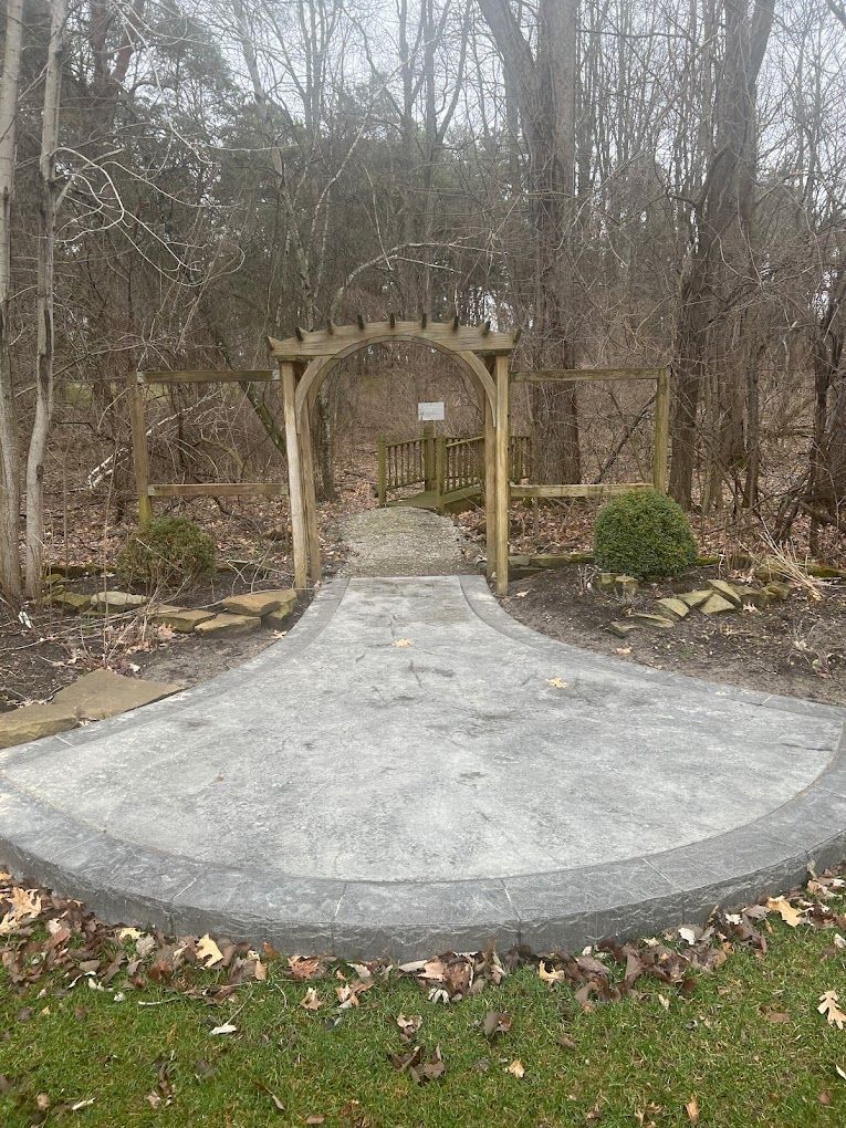 A patio with a wooden archway in the middle of a forest.