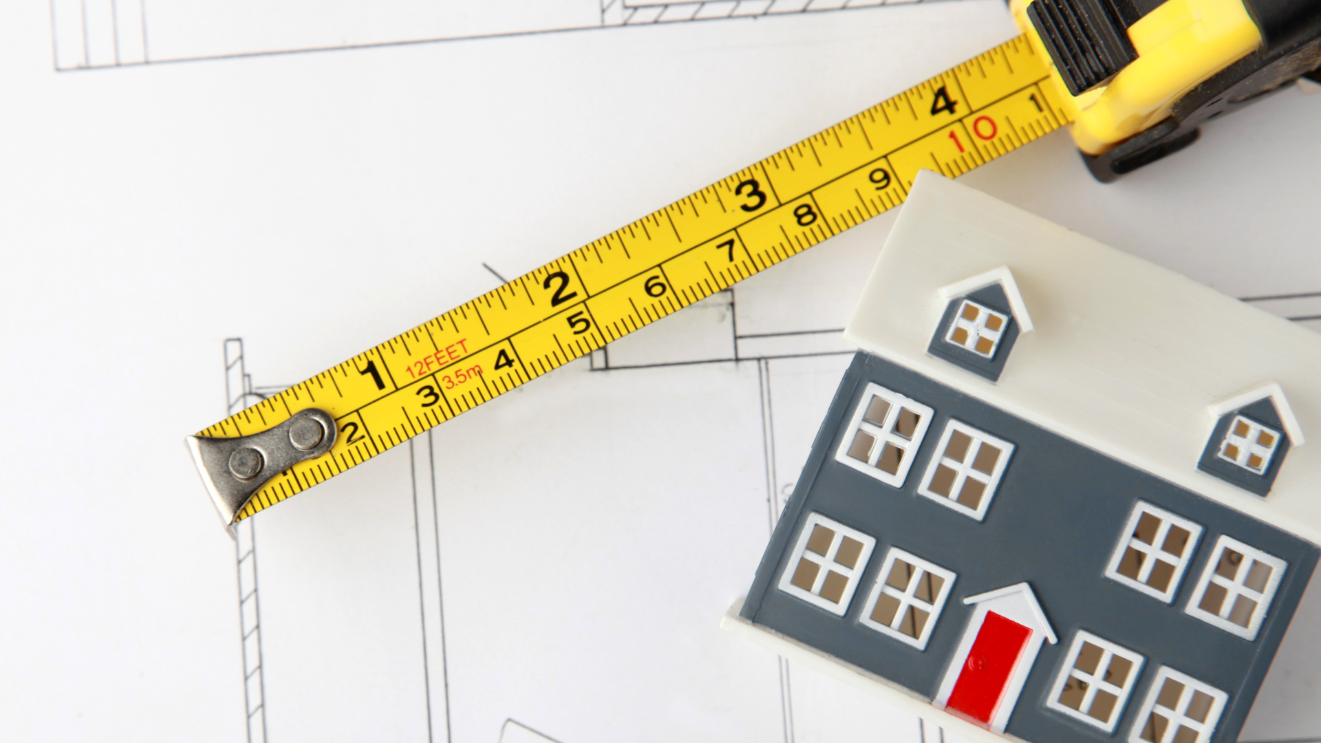 A measuring tape is laying on top of a model house.