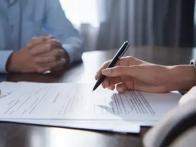 A person is sitting at a table signing a document with a pen.
