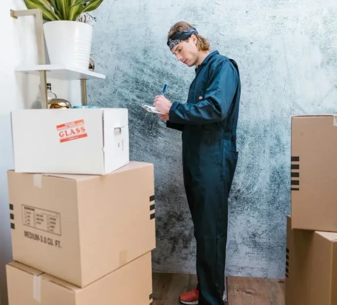 A mover checking a clipboard inventory next to packed glass boxes.