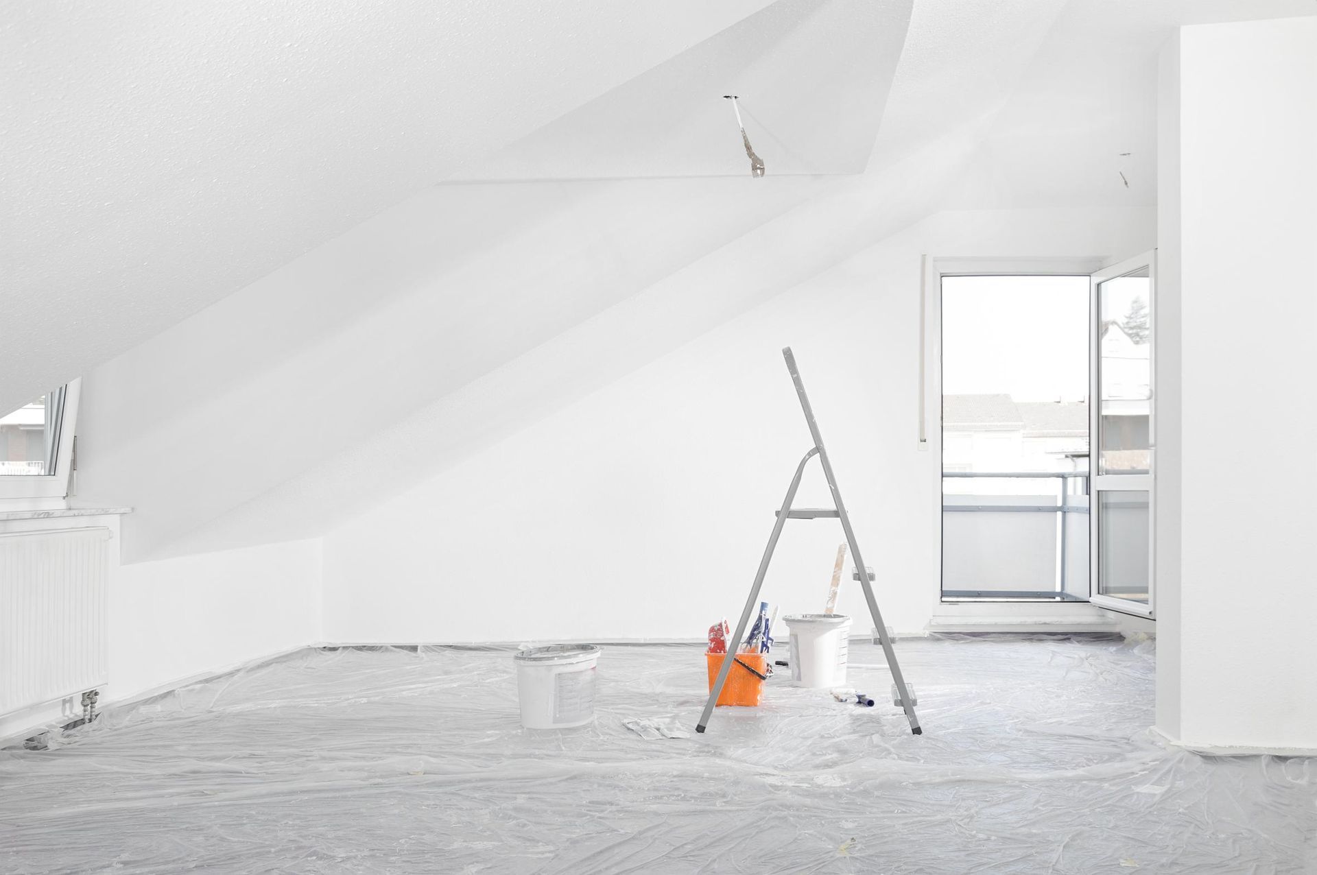 Room with white walls and ceiling, painting equipment, and ladder.