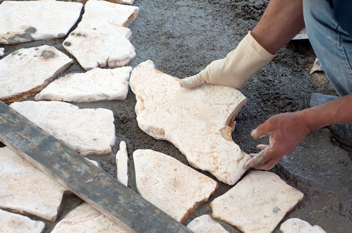 Person in gloves placing irregularly shaped stone on wet mortar.