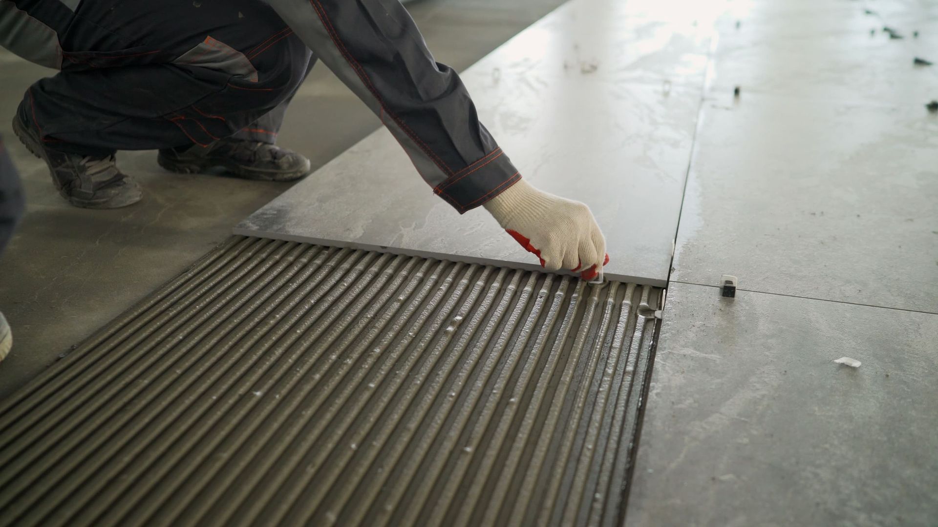 Person installing large floor tiles, using a notched trowel to spread adhesive.