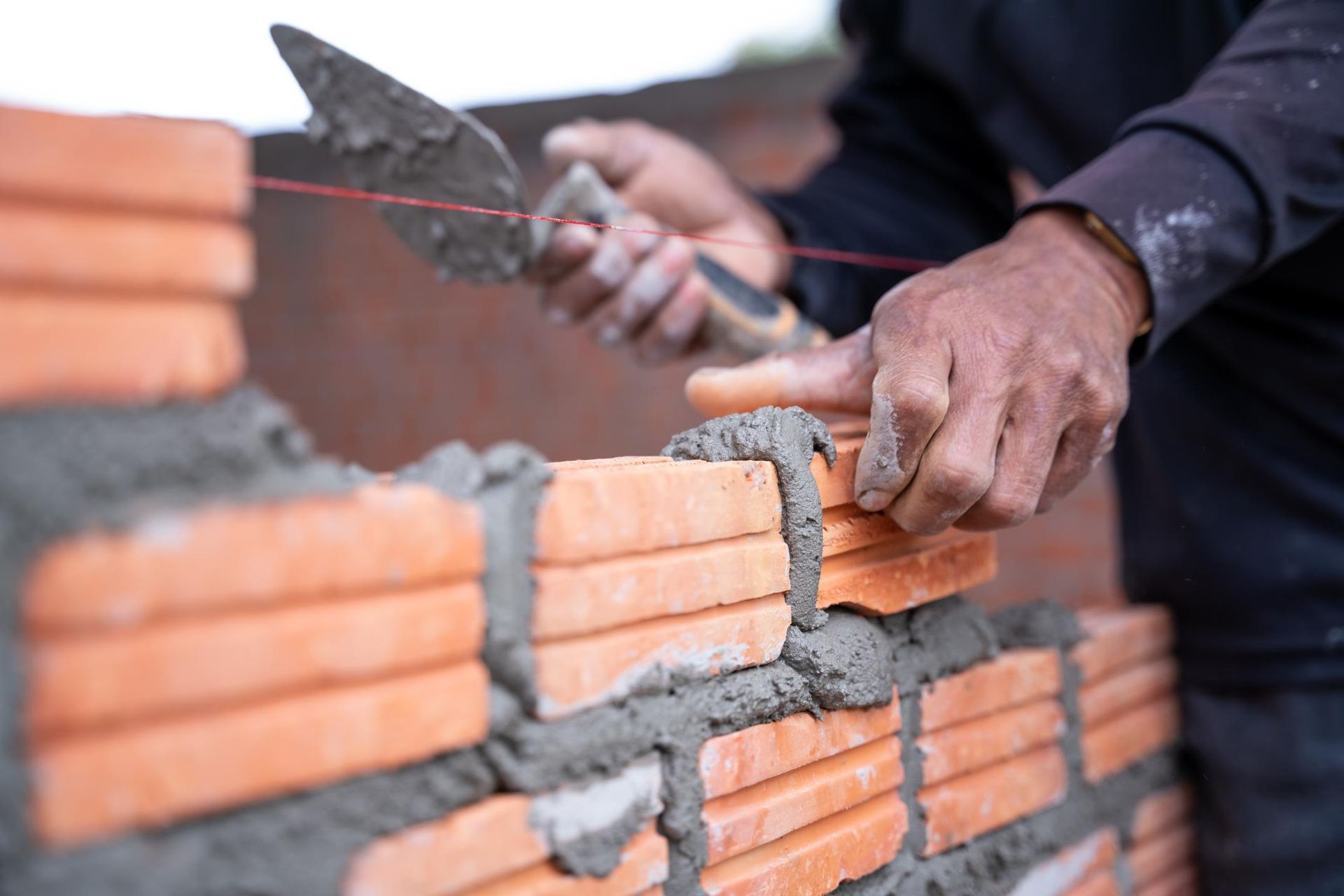 Bricklayer using a trowel to apply mortar on bricks, building a wall.