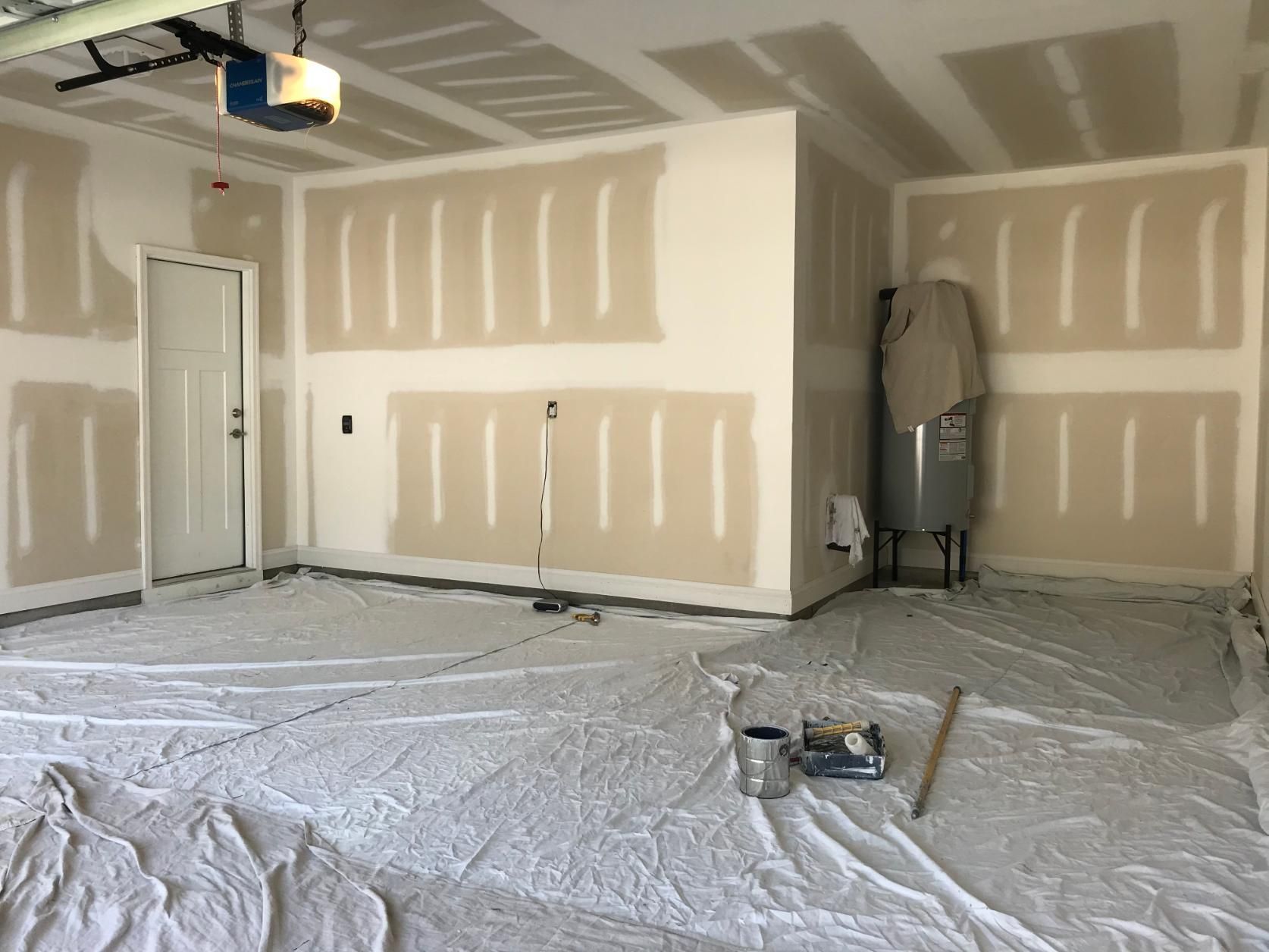 Garage interior with drywall partially installed, covered in protective sheeting, ready for painting.