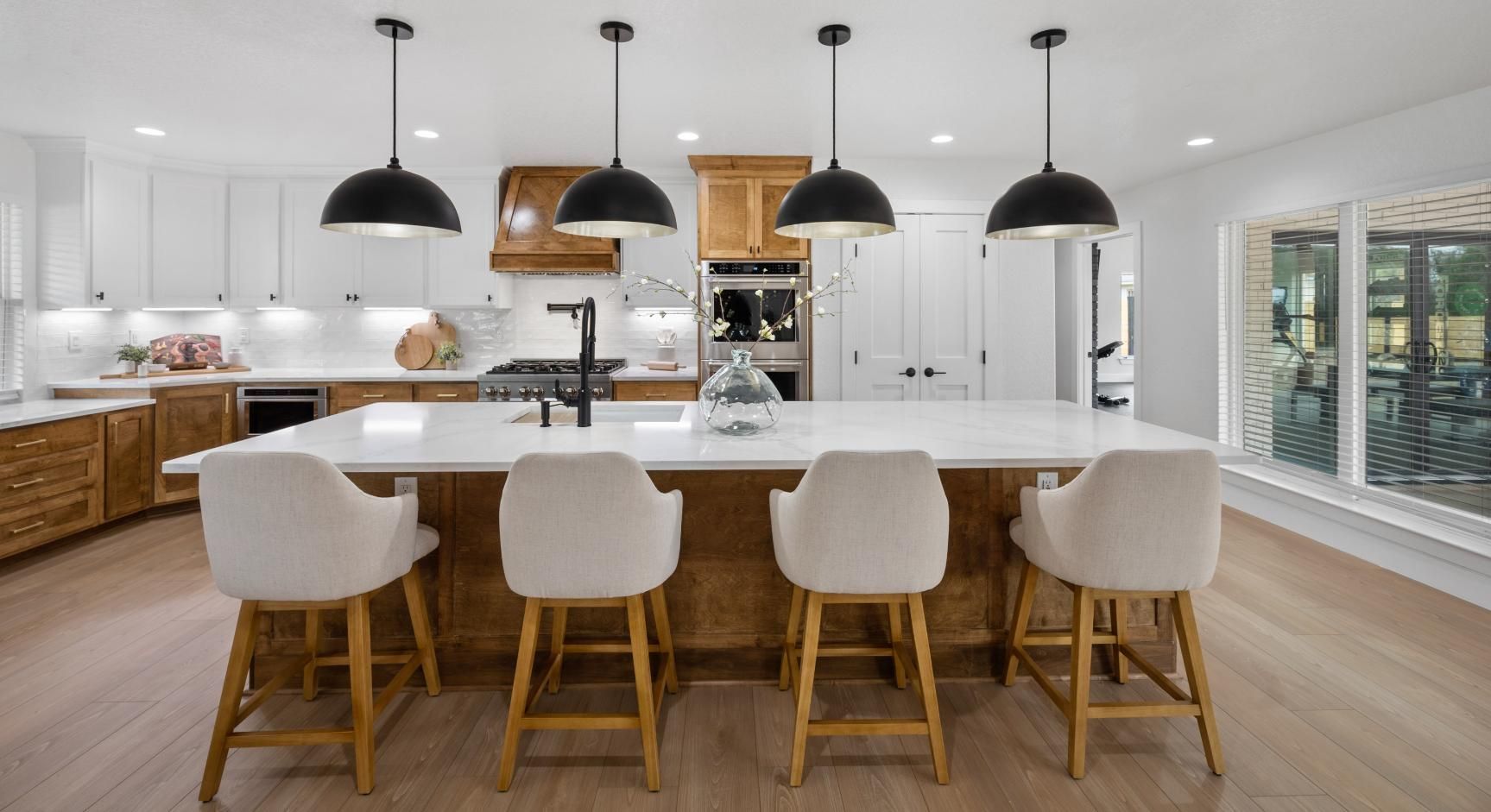 Modern kitchen with island, white countertops, four black pendant lights, and light wood cabinetry.