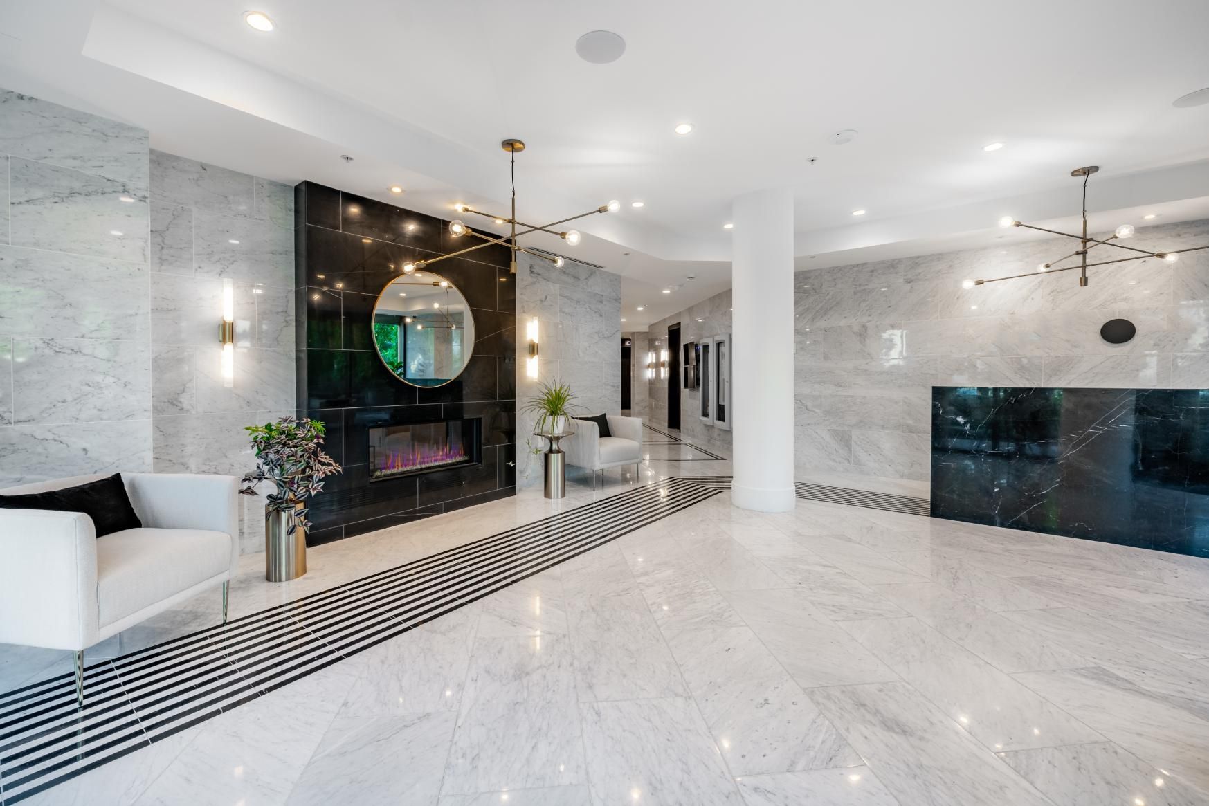 Luxurious lobby with marble walls and floors, fireplace, gold lighting, and a small sofa.