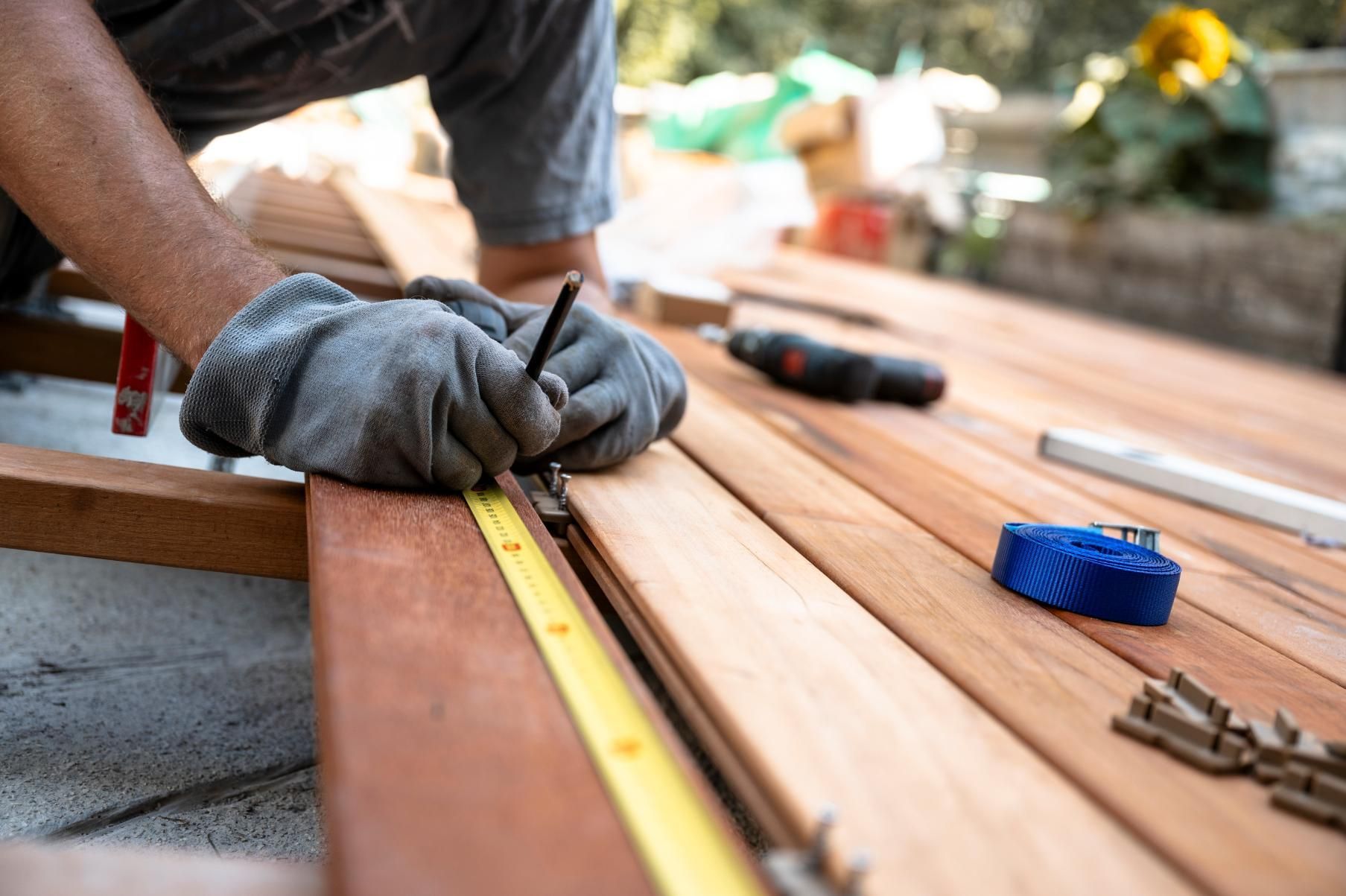 Person wearing work gloves marks wood with a pencil and measuring tape for deck construction.