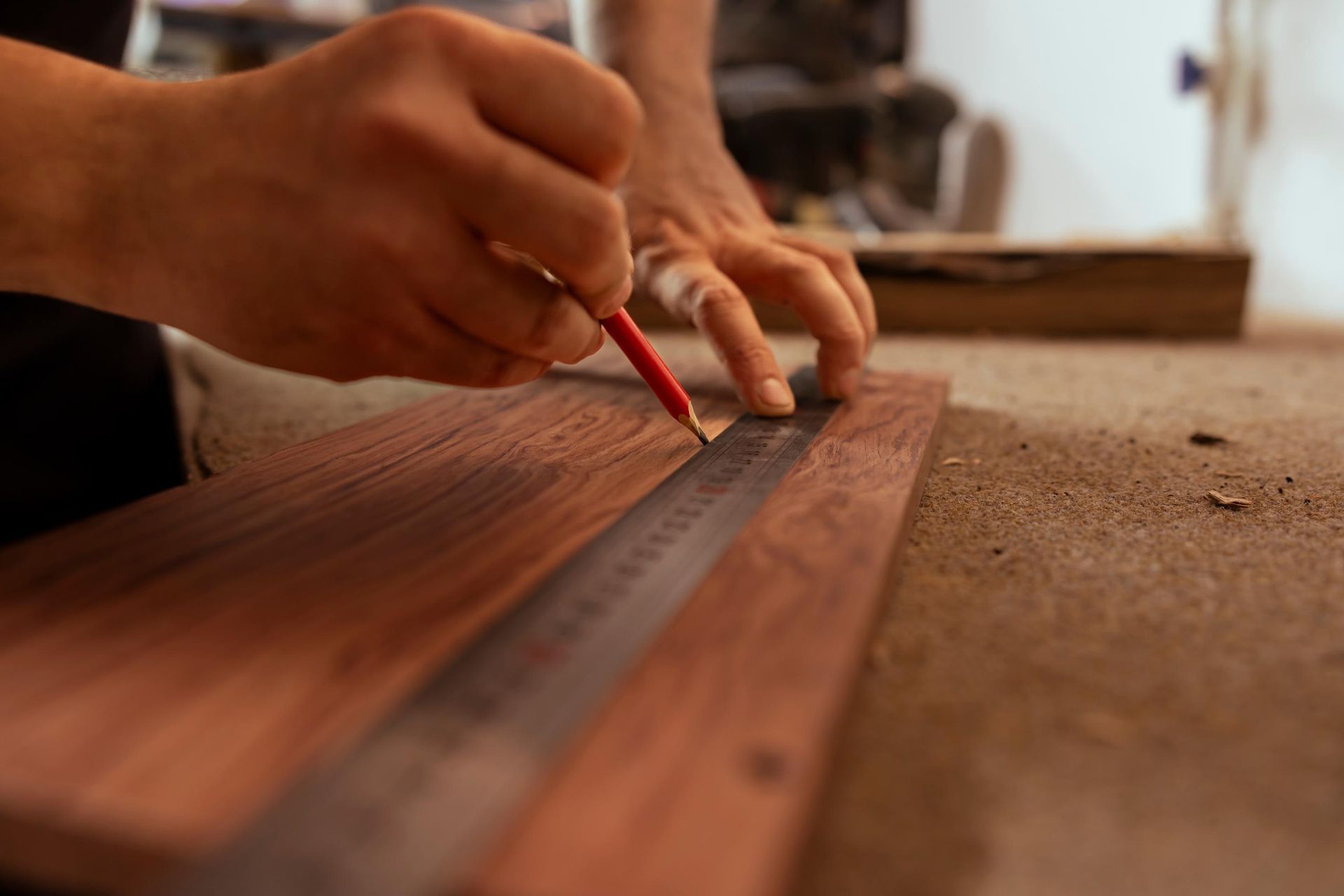 Person using a pencil and ruler to mark a wooden board in a workshop.