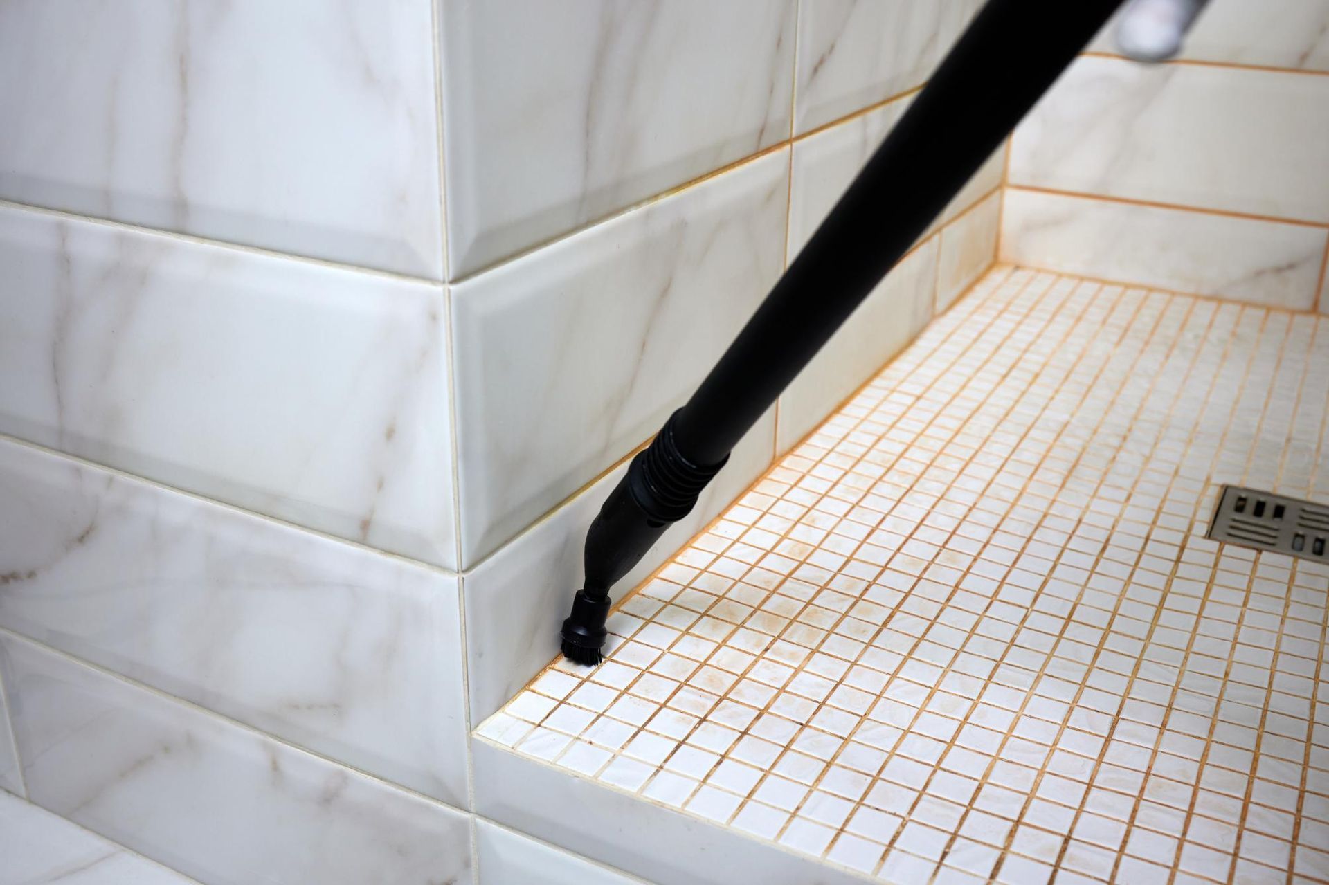Steam cleaner cleaning a tiled shower floor and wall.